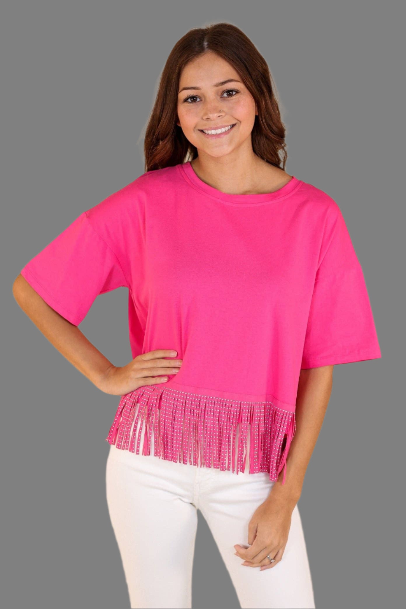 Woman wearing a bright pink top with fringe details on a beige background